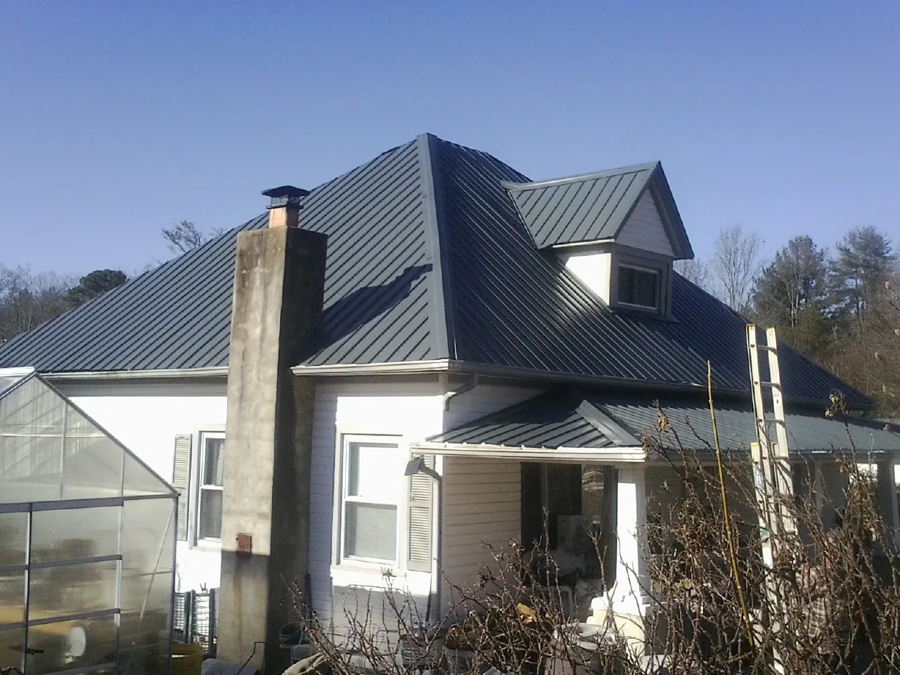 Dark blue standing seam metal roof on a white farmhouse with dormer — Slate & Tile Roof Repair by Roofing Brothers in Alfred