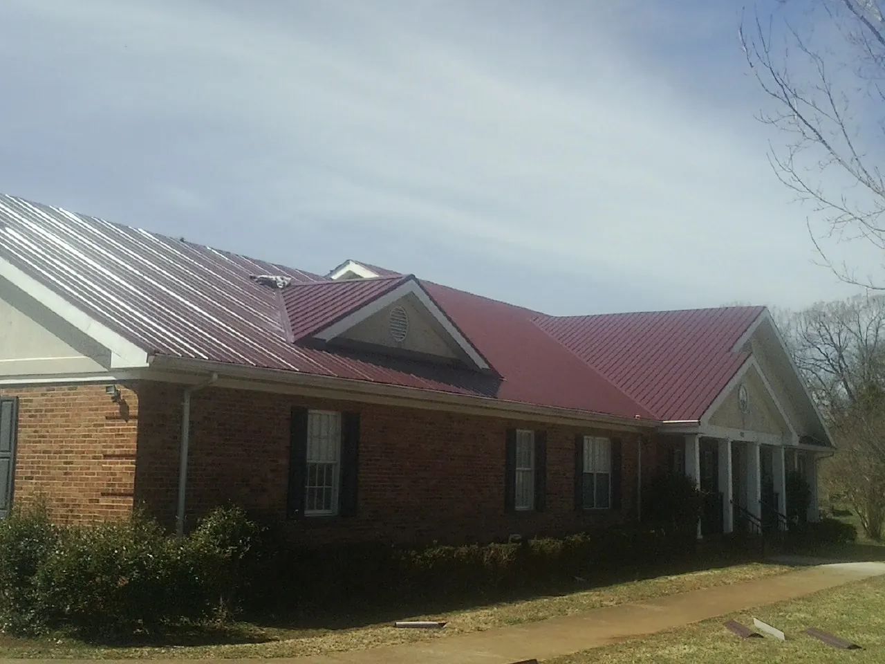 Red metal roof with gabled entries on a long brick building, from a Hail Damage Roof Repair job in Alfred