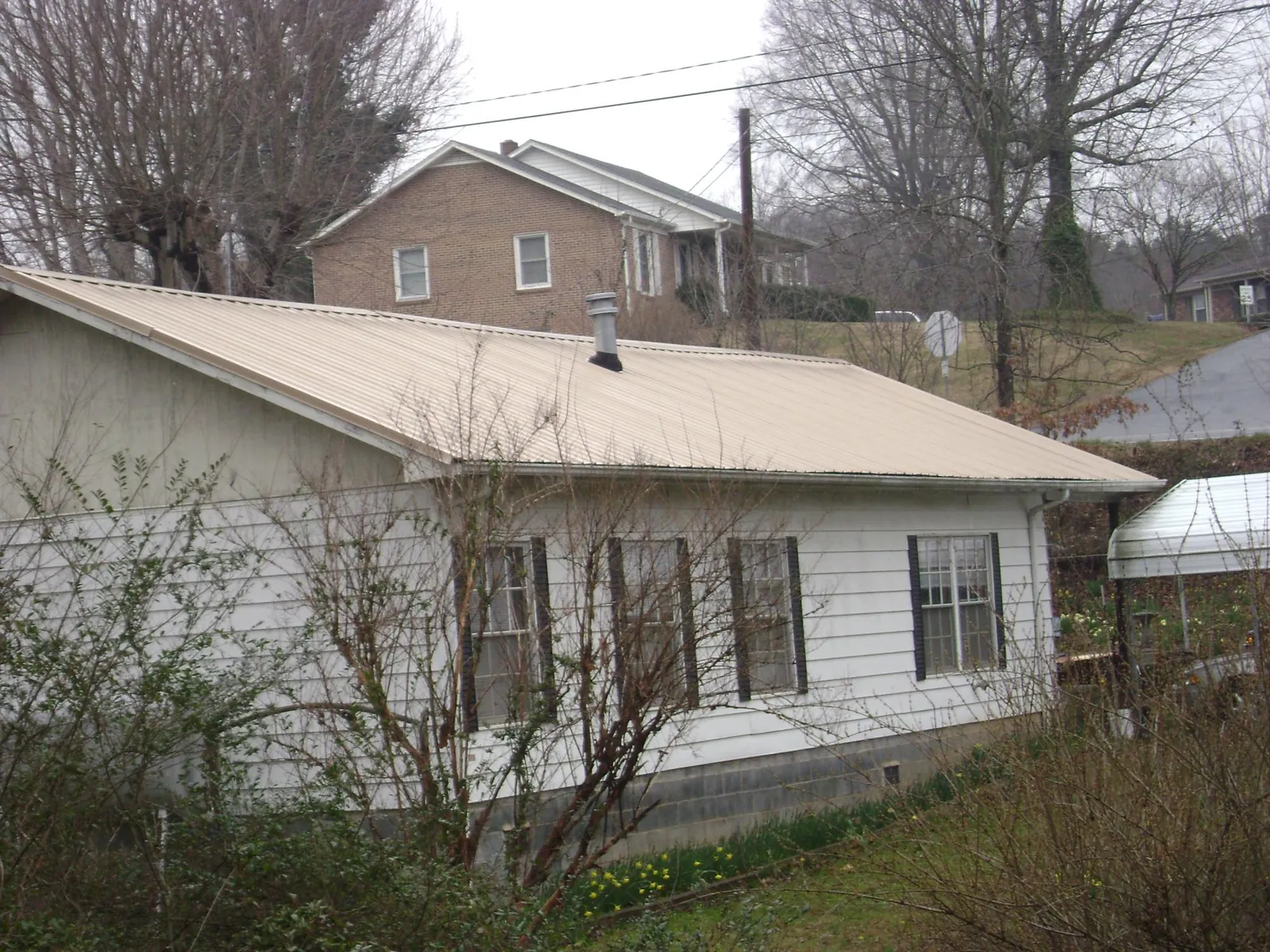 Tan metal roof on a white sided house set into a hillside — Commercial Roofing by Roofing Brothers in Alfred