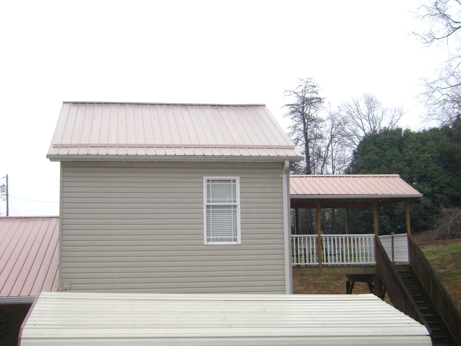 Tan metal roofs on a two story addition and attached porch, from a Roof Replacement job in Alfred